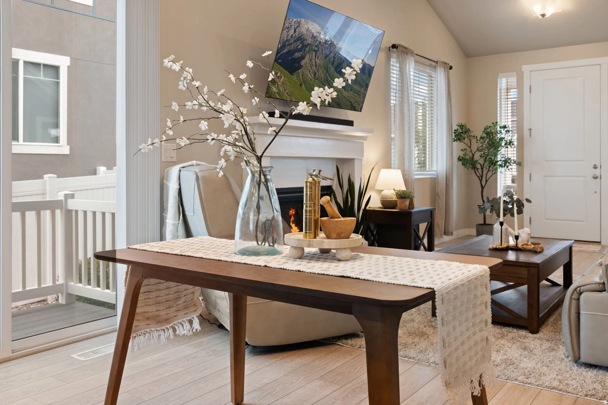 Fireplace with a white mantel, vaulted ceiling, wood-finish flooring, sliding glass door, and white paneled entry door