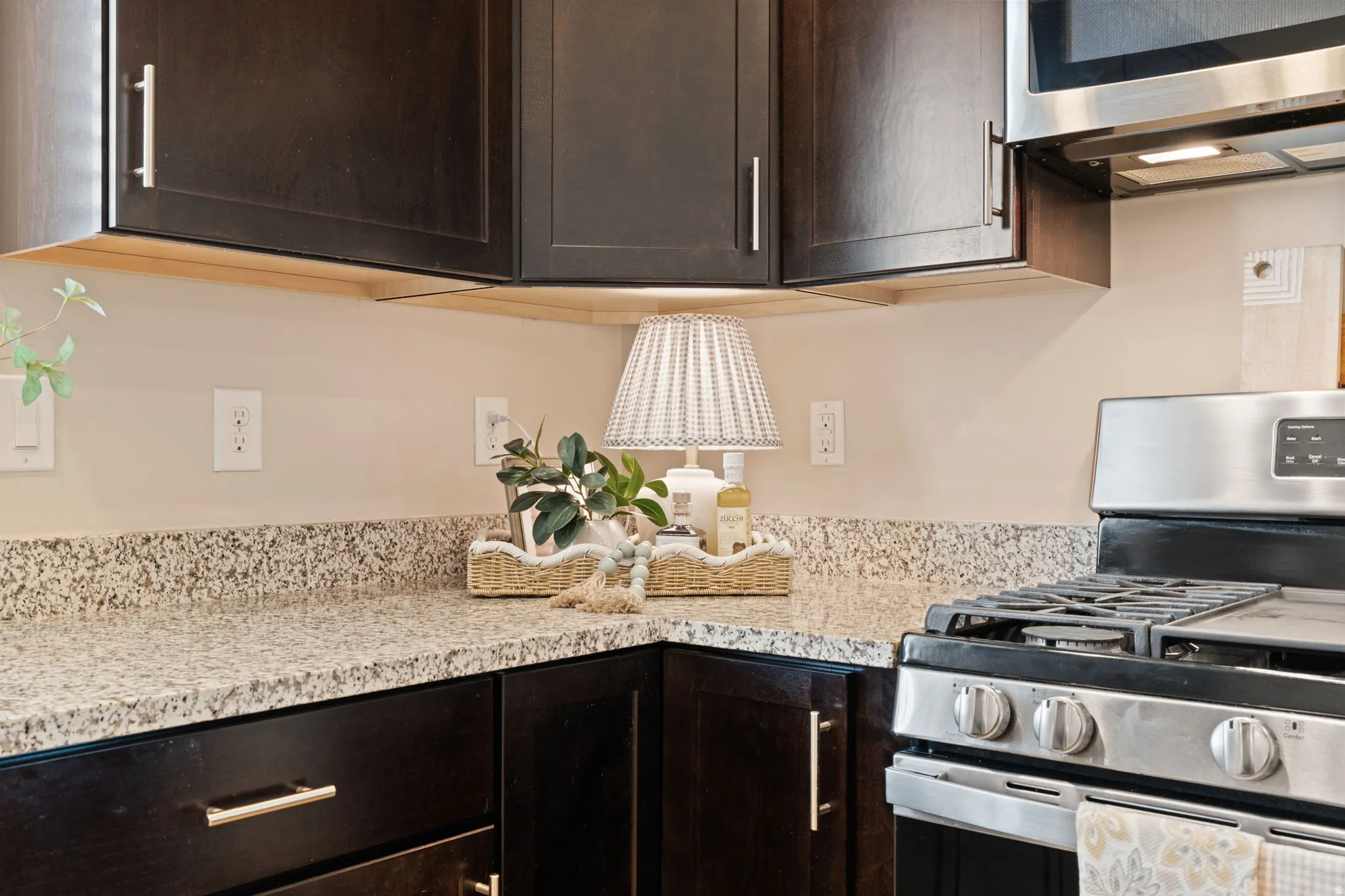 Dark wood-finish cabinetry with silver hardware, speckled stone countertops, and a stainless steel range with overhead microwave