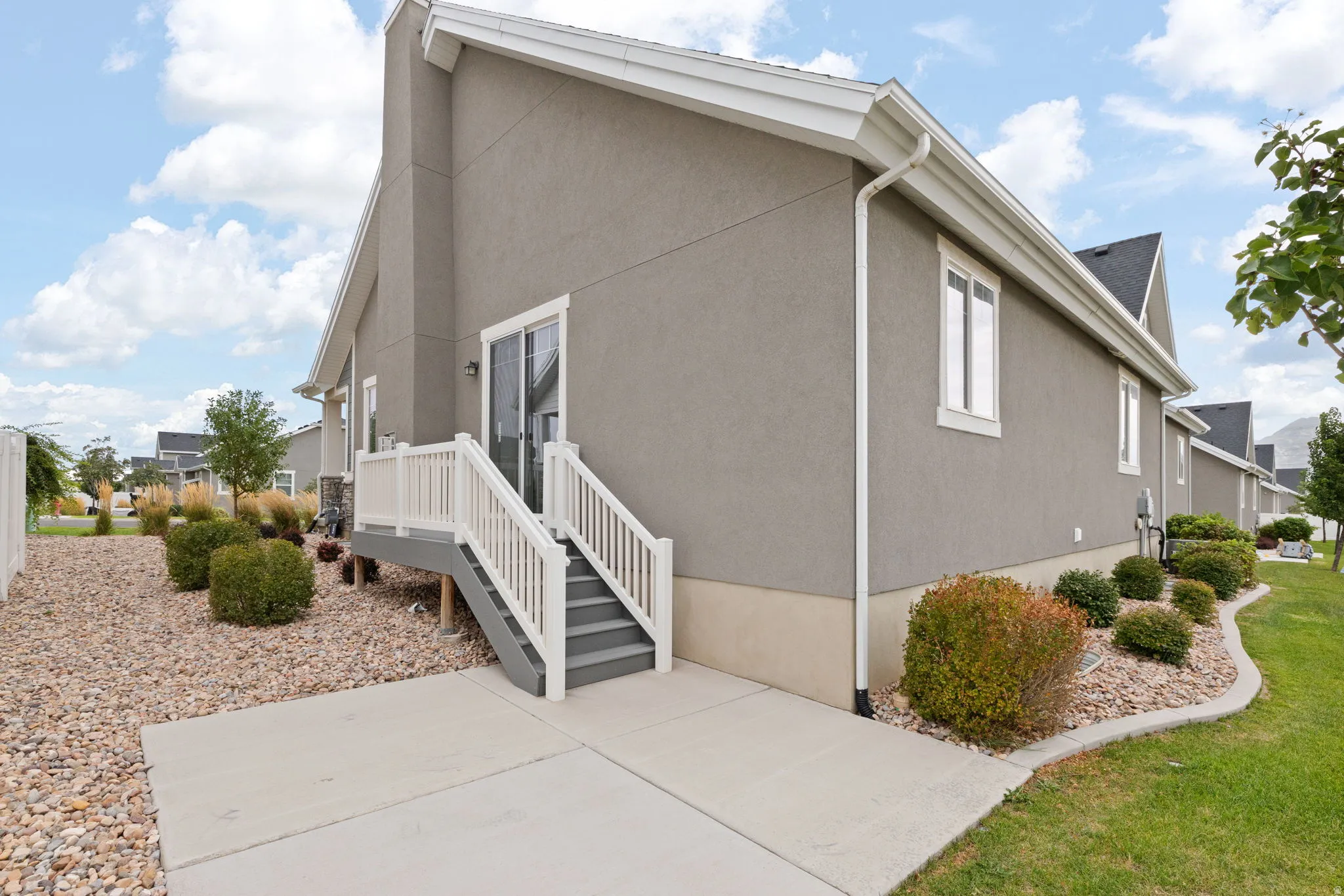 Exterior featuring stucco siding, white-framed windows, a concrete patio, and a deck with white railings
