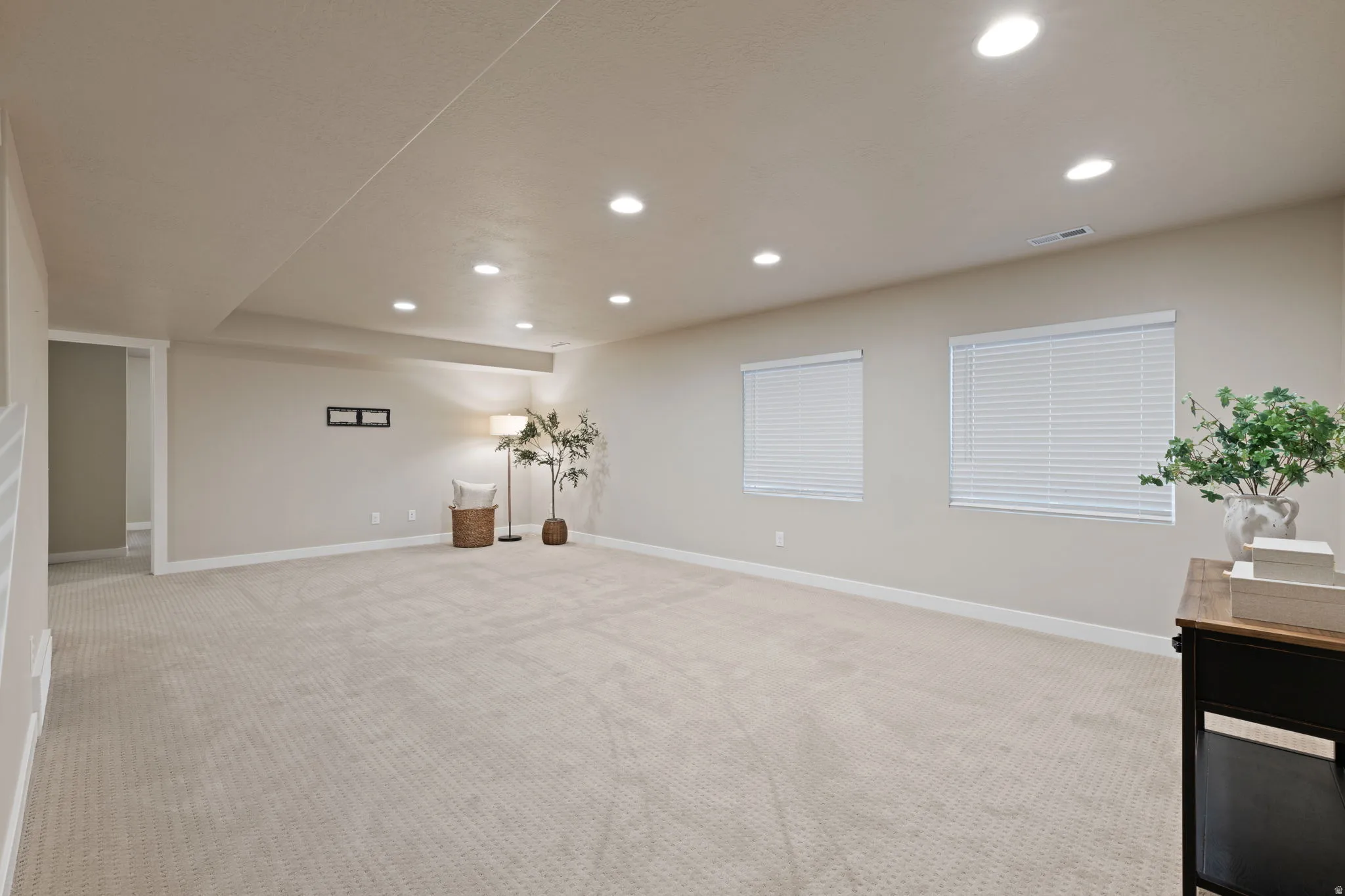 Recessed lighting throughout, two windows with blinds, light-toned wall paint, and carpeted flooring