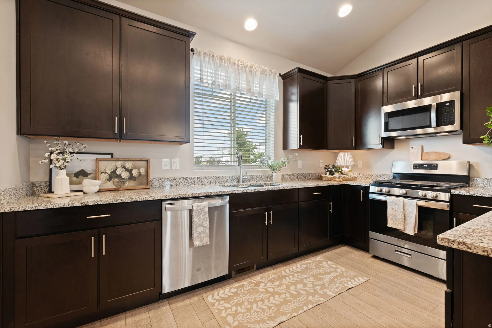Kitchen featuring dark wood-finish cabinetry, light speckled countertops, stainless steel appliances, and a tile floor