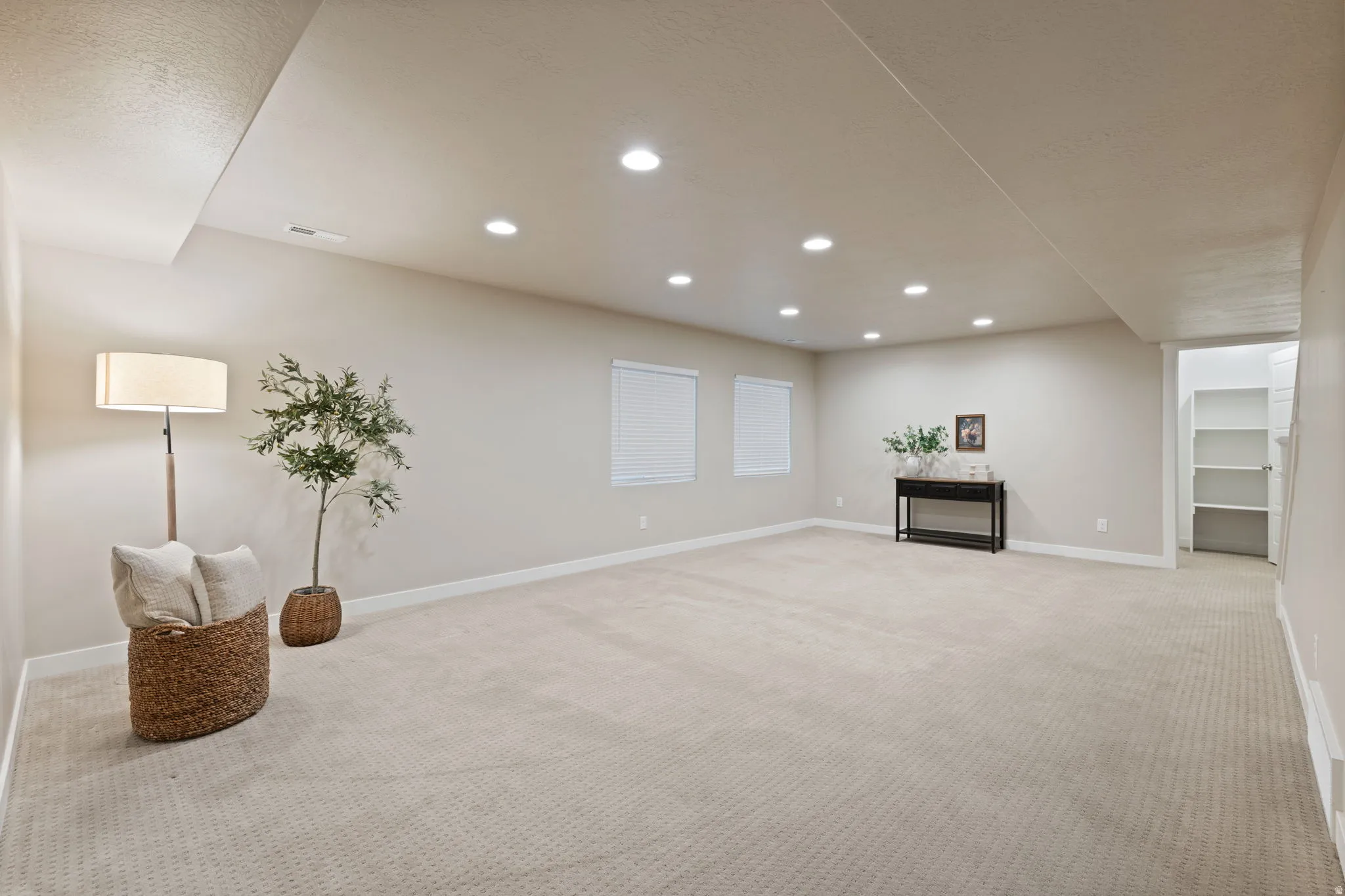 Expansive carpeted area with recessed lighting, two windows, and built-in shelving
