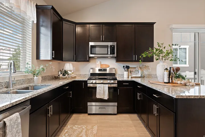 U-shaped kitchen with dark wood cabinetry, light speckled countertops, stainless steel appliances, and wood-finish flooring