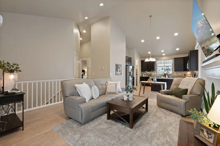 Open-concept living space featuring high ceilings, recessed lighting, wood-finish flooring, a white railing, and a kitchen with dark cabinetry and stainless steel appliances