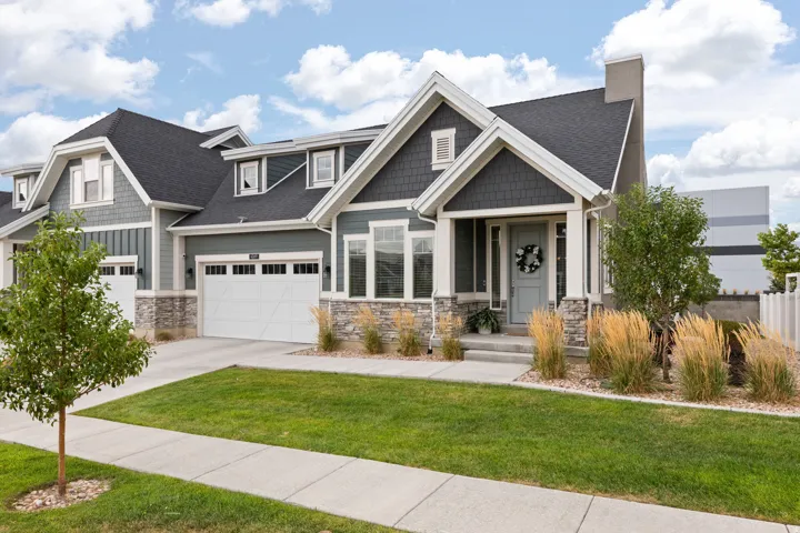 Crafted exterior featuring stone and shake siding accents, an attached two-car garage, covered porch entry, and a manicured lawn