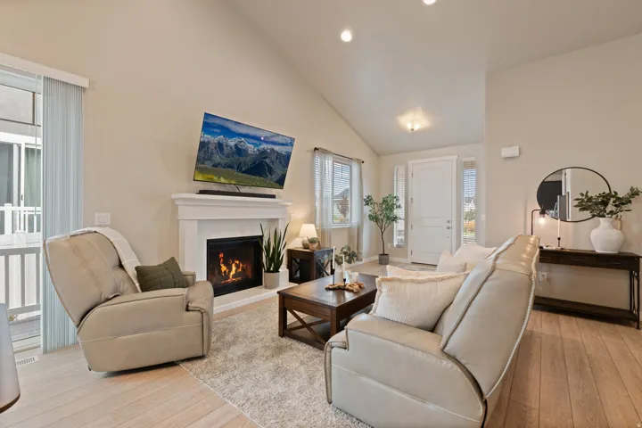 Vaulted ceiling living area featuring a fireplace with a white mantel, light wood-finish flooring, and recessed lighting