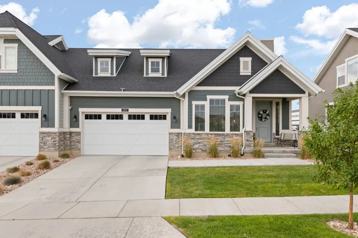 Contemporary exterior with mixed material facade, stone accents, two-car garage, covered porch, and front lawn