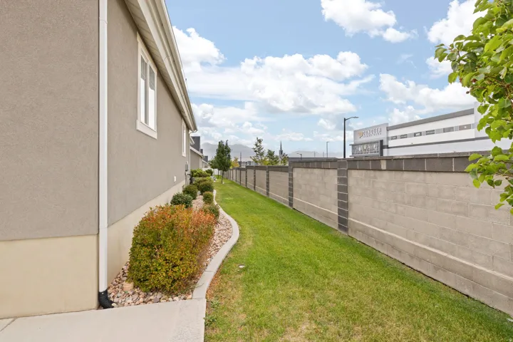 Landscaped side yard featuring a stucco exterior, concrete foundation, manicured lawn, and a block perimeter wall