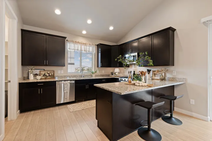 Kitchen featuring wood-finish flooring, dark wood cabinetry, granite countertops, stainless steel appliances, and recessed lighting