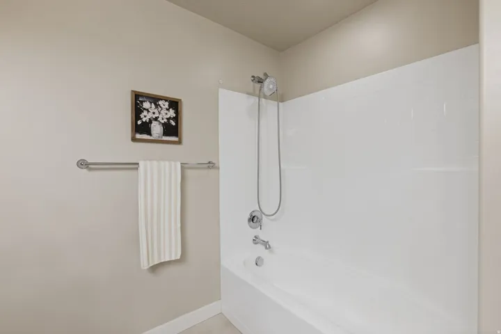 Bathtub with a white tile-patterned surround, chrome fixtures, and a hand-held showerhead
