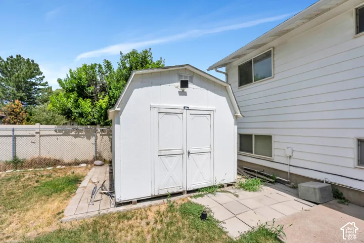 White outdoor storage shed with double doors, concrete slab foundation, and chain-link fencing