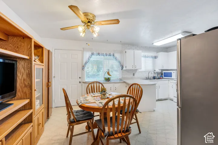 White cabinetry, subway tile backsplash, stainless steel refrigerator, ceiling fan with integrated lighting, and built-in wood-finish shelving
