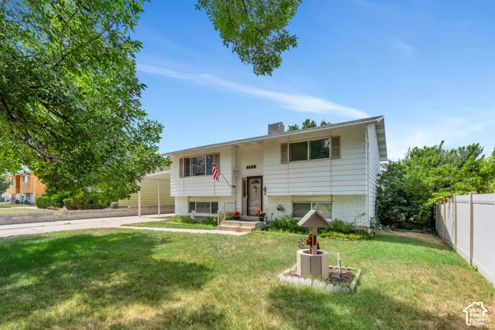 Split-level residence featuring a white exterior, attached carport, and a well-maintained lawn