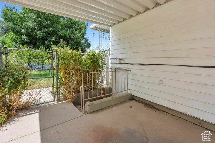 Covered patio with concrete surface, white siding, and a chain-link fence