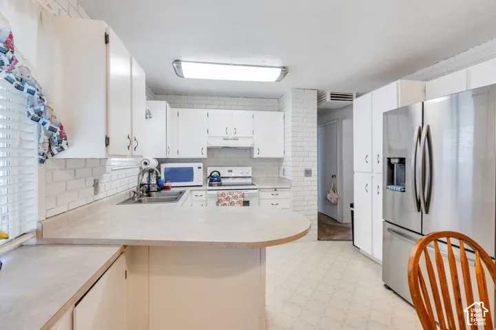 White cabinetry with brushed nickel hardware, light-toned countertops, white subway tile backsplash, stainless steel refrigerator, and patterned flooring