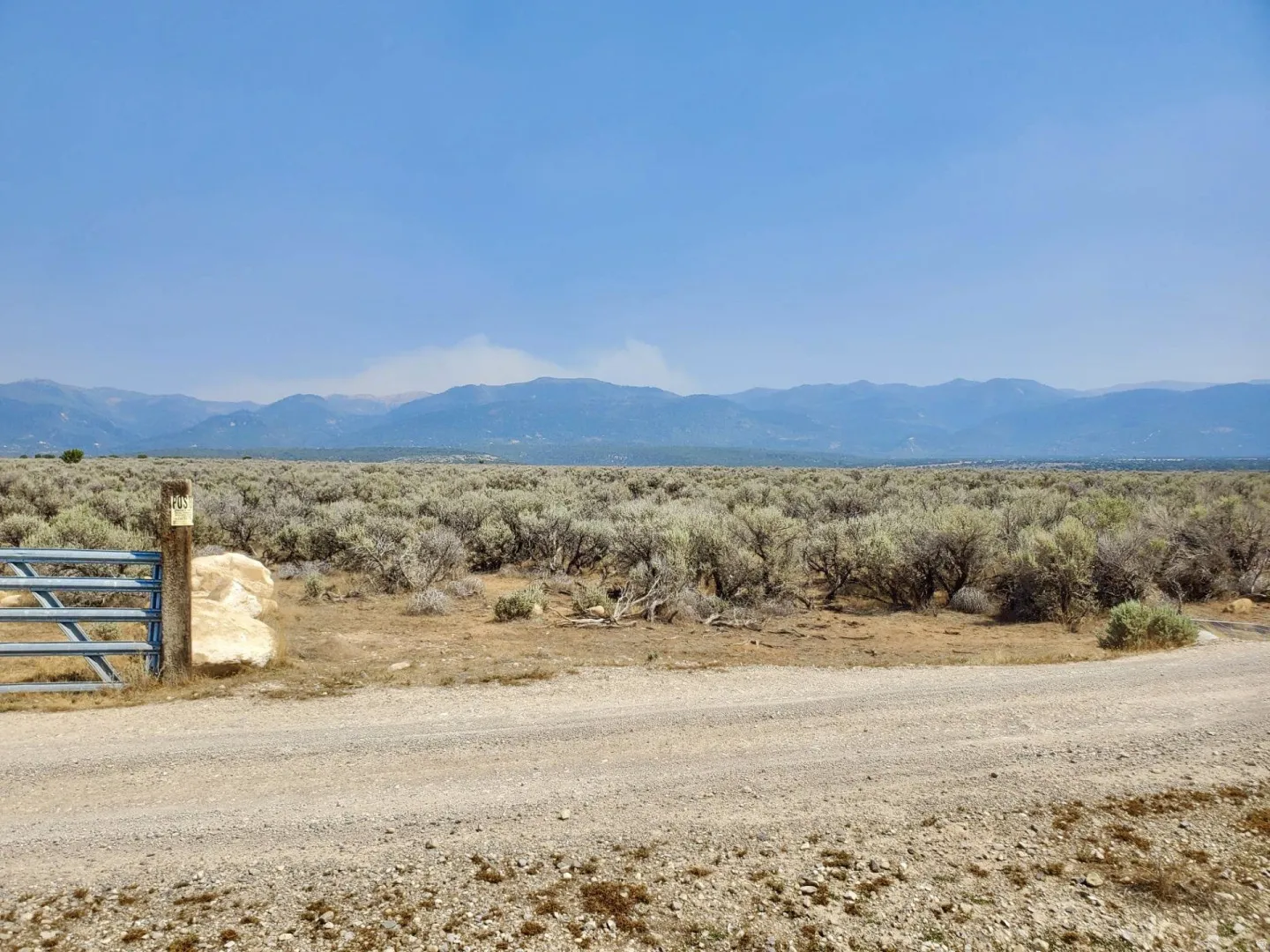 Expansive terrain featuring a gravel road, natural brush, and a metal gate