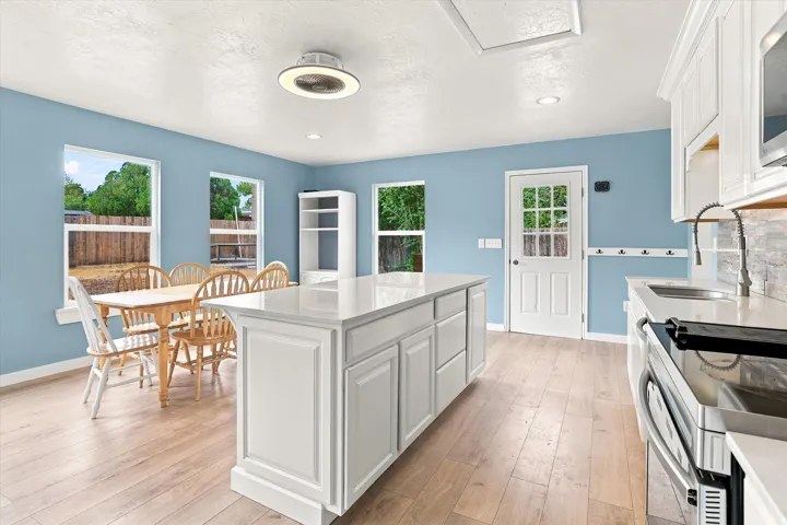 Kitchen featuring a center island with countertop, wood-finish flooring, white cabinetry, integrated sink, and stainless steel appliances