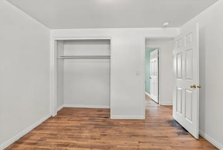 Wood-finish flooring, white walls, and a built-in closet with a hanging rod