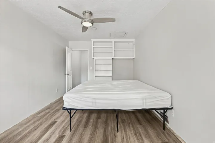 Wood-finish flooring, built-in shelving, white paneled door, and a ceiling fan with integrated lighting