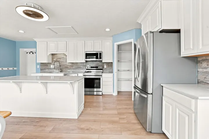 Kitchen featuring wood-finish flooring, white cabinetry, a central island with a solid surface countertop, stainless steel appliances, and a stone-finish backsplash