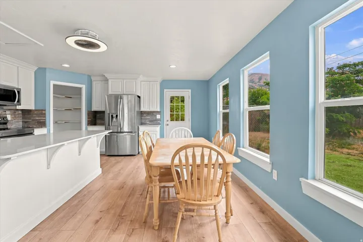 Light wood-finish flooring, white cabinetry, integrated stainless steel appliances, stone-tile backsplash, and multiple windows