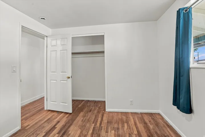 Wood-finish flooring, white painted walls, window with trim, recessed ceiling lighting, and built-in closet with rod and shelf
