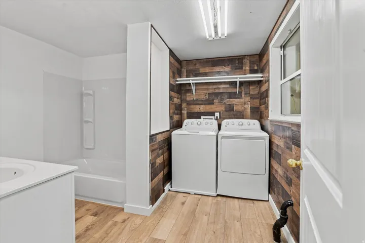 White appliances, wood-finish flooring, built-in shelving, white bathtub with integrated shower, white vanity