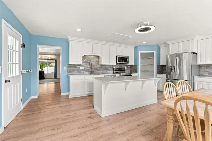 Kitchen featuring light wood-finish flooring, white cabinetry, a central island, stainless steel appliances, and a tiled backsplash