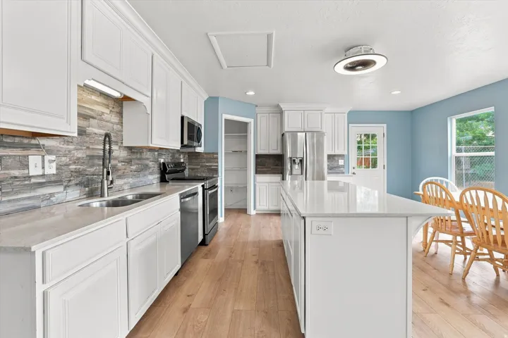 Kitchen featuring white cabinetry, stone-finish backsplash, stainless steel appliances, a center island with a light-toned countertop, and wood-finish flooring