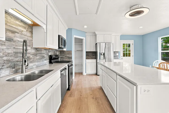 Modern kitchen featuring light wood-finish flooring, white cabinetry, integrated stainless steel appliances, and a kitchen island with a light-colored countertop