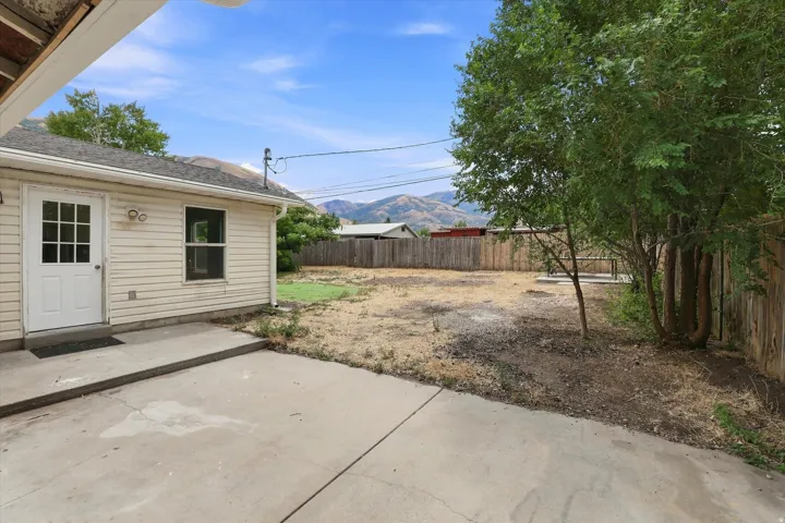Expansive backyard with a concrete patio, mature trees, and privacy fencing