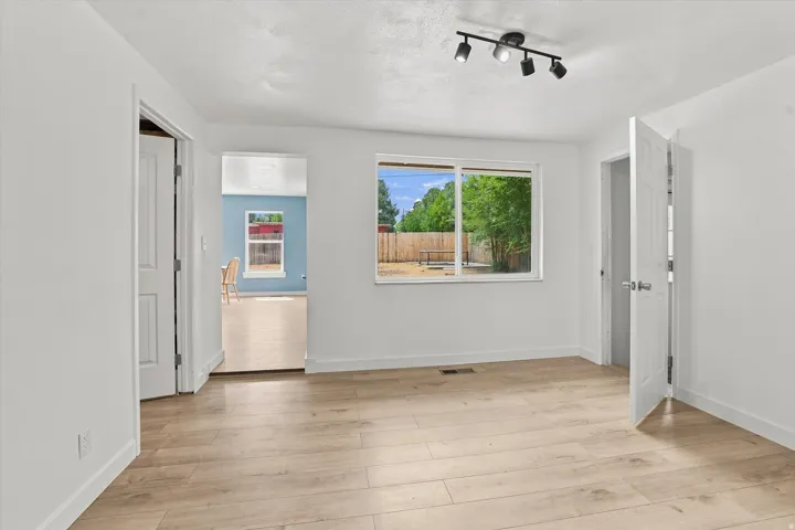 Light wood-finish flooring, white walls, modern track lighting, and a window overlooking the backyard