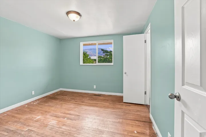 Hardwood flooring, light blue wall paint, white trim, recessed window with exterior scenery, and a white paneled door