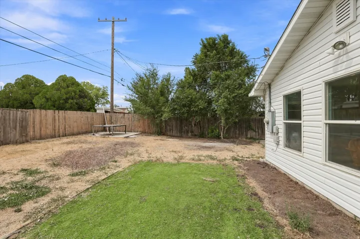 Enclosed backyard featuring a wood privacy fence, partial grass lawn, and a concrete patio