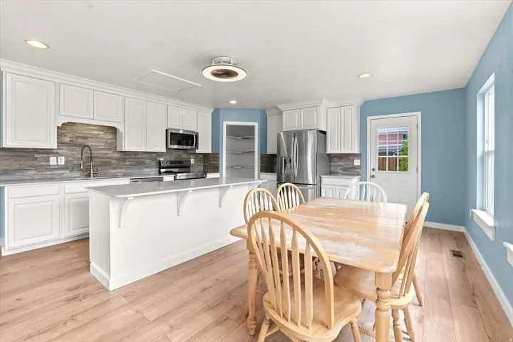 White cabinetry, stainless steel appliances, central island, wood-finish flooring, and a glass-paneled exterior door