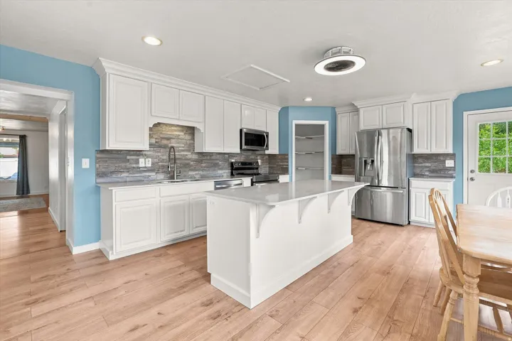 Kitchen featuring wood-finish flooring, white cabinetry, a central island, stainless steel appliances, and a tiled backsplash