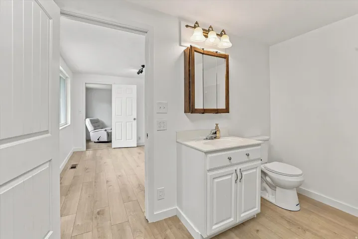 Wood-finish flooring throughout, white vanity with integrated sink, wood-framed medicine cabinet, and three-light vanity fixture