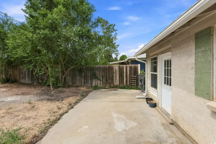 Concrete patio with a white paneled door, a single-pane window, and a wood privacy fence