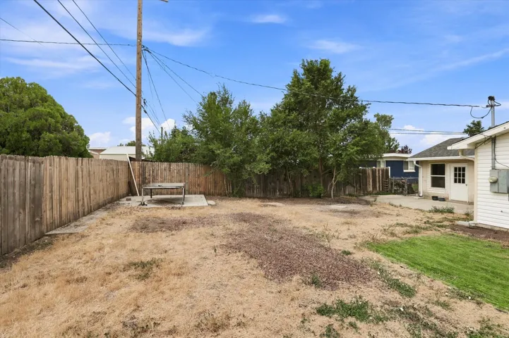 Expansive backyard featuring a wood privacy fence, mature trees, concrete patio, and a separate building with siding and a white door