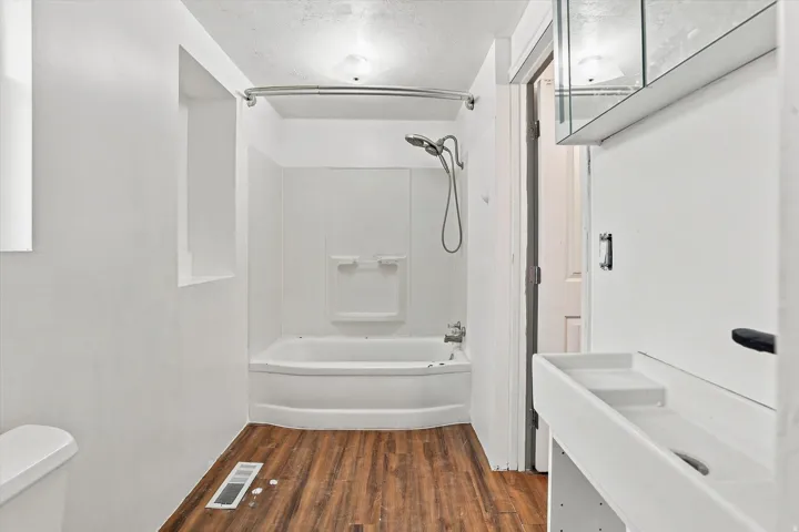 White bathtub with an integrated shower, wood-finish flooring, and a wall-mounted medicine cabinet