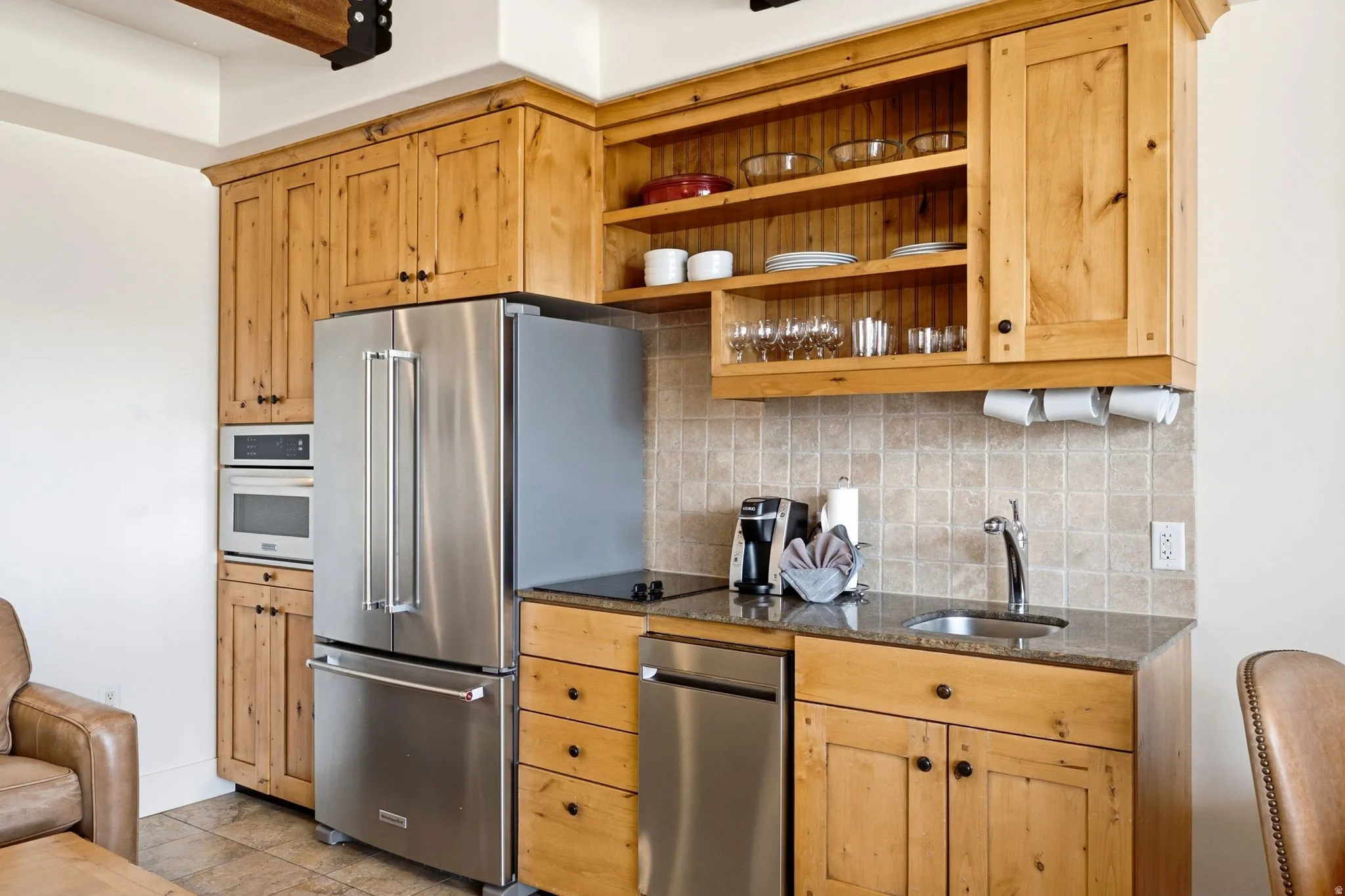 Stainless steel appliances, wood cabinetry, granite-style countertops, tile flooring, and a tile backsplash