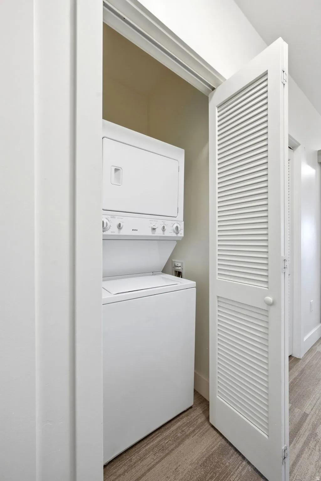 Stacked washer and dryer unit, louvered bi-fold closet doors, and wood-finish flooring