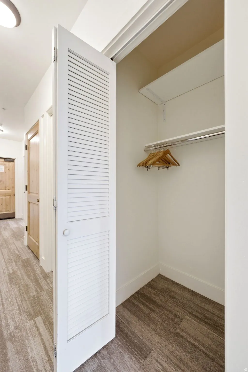 Louvered bi-fold doors opening to a closet with integrated shelving and a chrome hanging rod