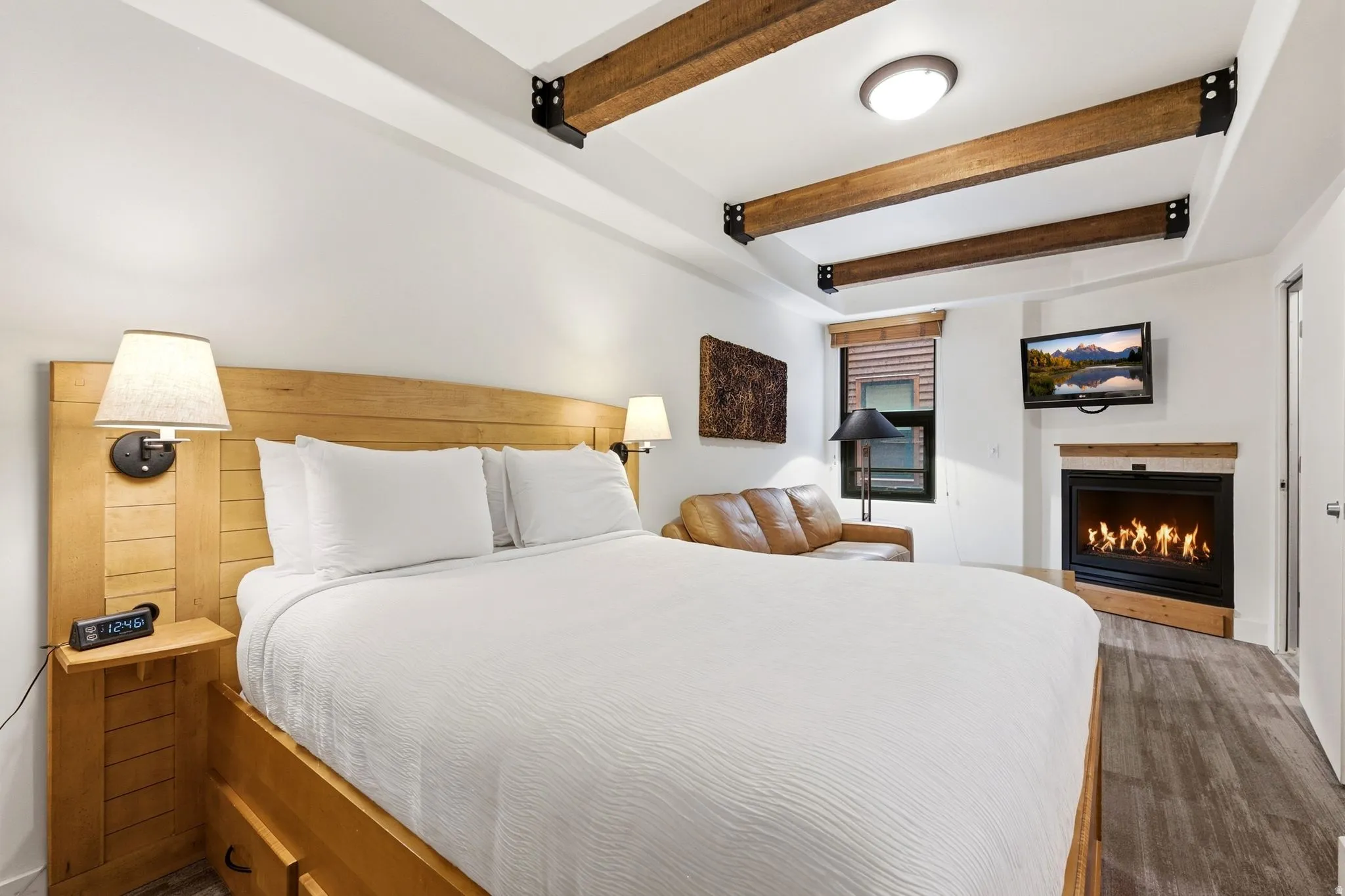 Wood-finish ceiling beams, built-in fireplace, wood-finish flooring, built-in wall sconces, and a built-in wood-finish headboard