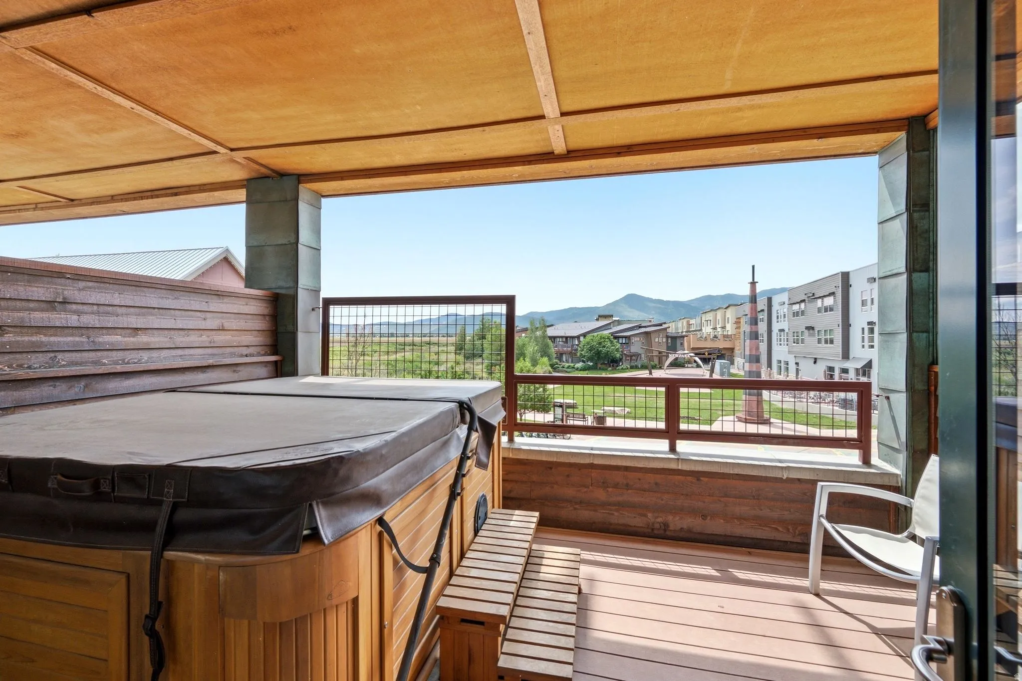 Covered outdoor deck with a hot tub and mountain scenery