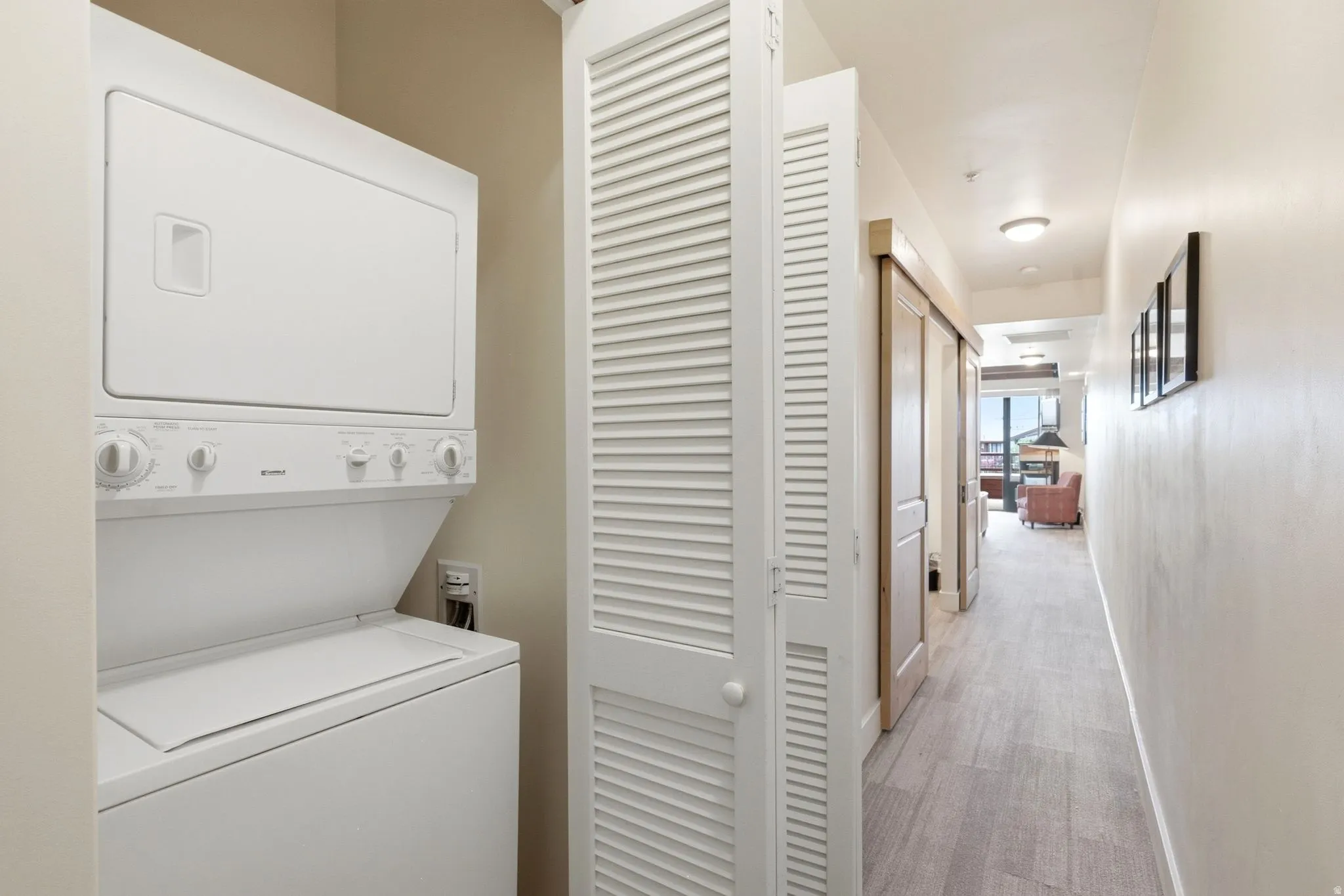 Stacked laundry appliances within a louvered closet, accompanied by wood-finish flooring and recessed lighting