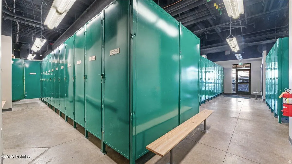 Extensive locker storage with durable green metal construction, concrete flooring, and suspended fluorescent lighting