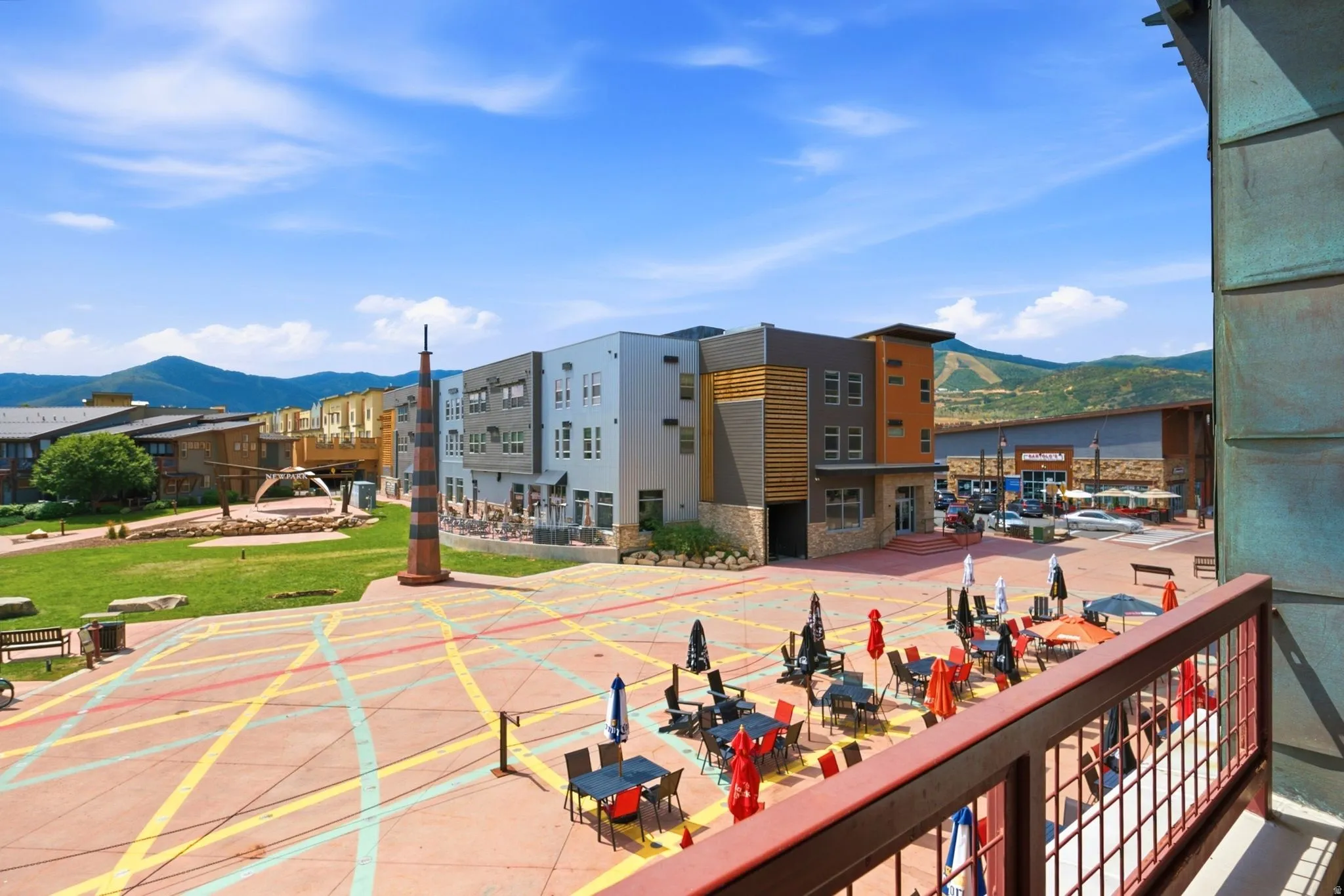 Balcony with metal railing overlooking a paved plaza with outdoor seating and a grassy area