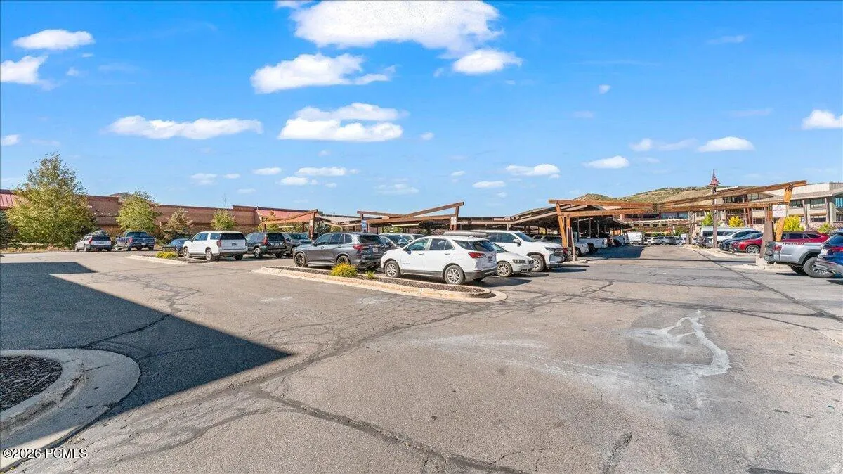 Paved parking lot with designated parking spaces, wood-frame shade structures, and an array of commercial buildings