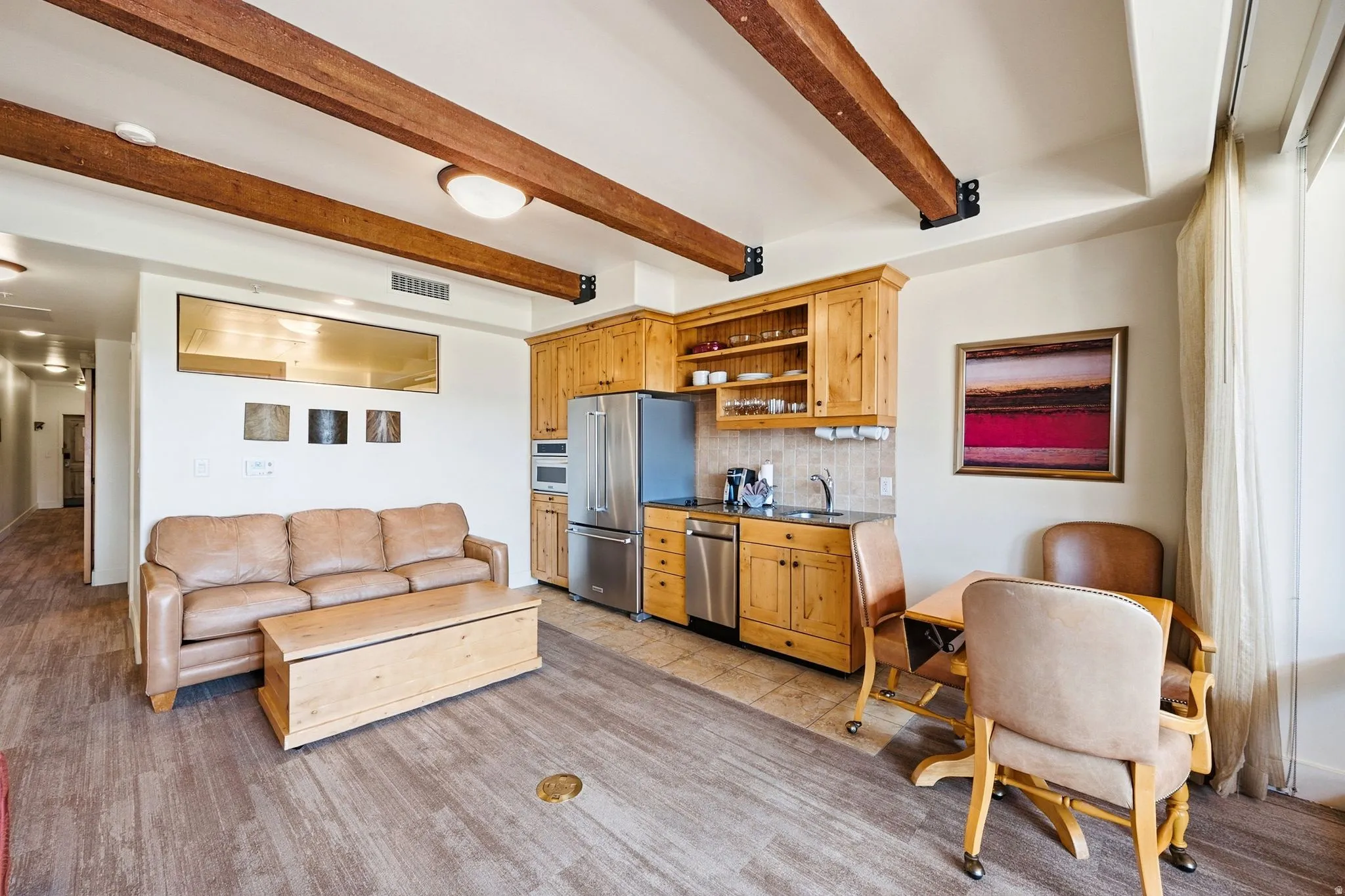 Exposed wood beams, wood-finish flooring, built-in kitchen cabinetry, stainless steel appliances, and a tiled kitchen backsplash